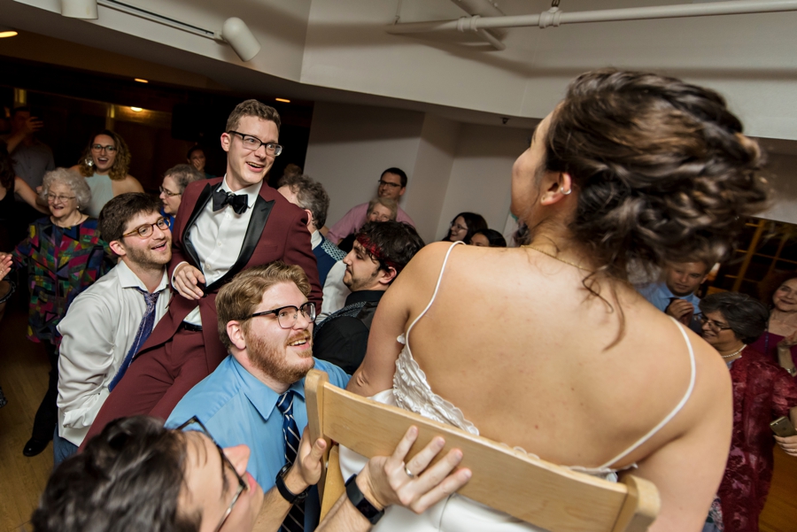 A bride and groom at a jewish wedding reception being lifted in chairs on the dance floor.